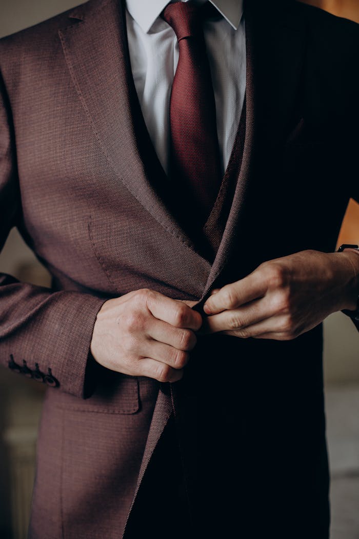 Close-up of a man in a burgundy suit adjusting his jacket, showcasing style and sophistication.