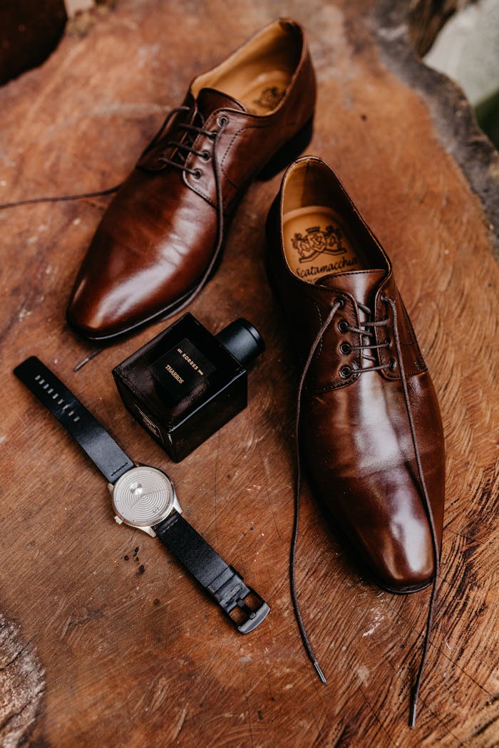 Stylish brown dress shoes, watch, and perfume bottle on rustic wood.